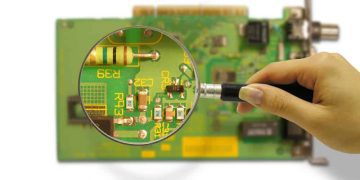 Person using a magnifying glass to look at a PCB