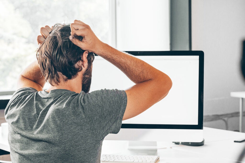 A frustrated electrical engineer holding his head in his hands while looking at a computer screen