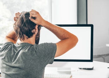 A frustrated electrical engineer holding his head in his hands while looking at a computer screen