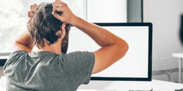 A frustrated electrical engineer holding his head in his hands while looking at a computer screen