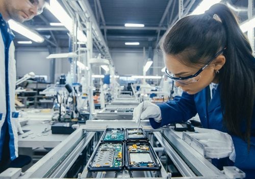 woman assembling PCB with coworker watching