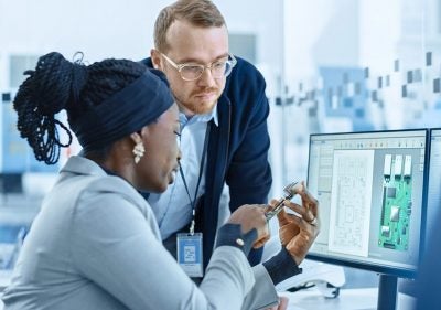 Coworkers reviewing physical PCB in front of computer